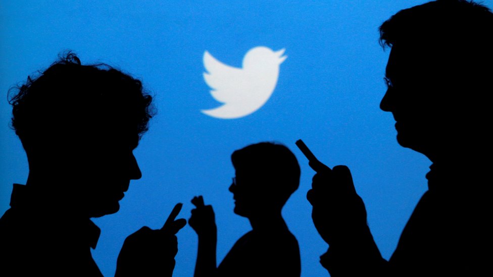 Twitter logo on a screen with the silhouettes of people on their phones in front of it