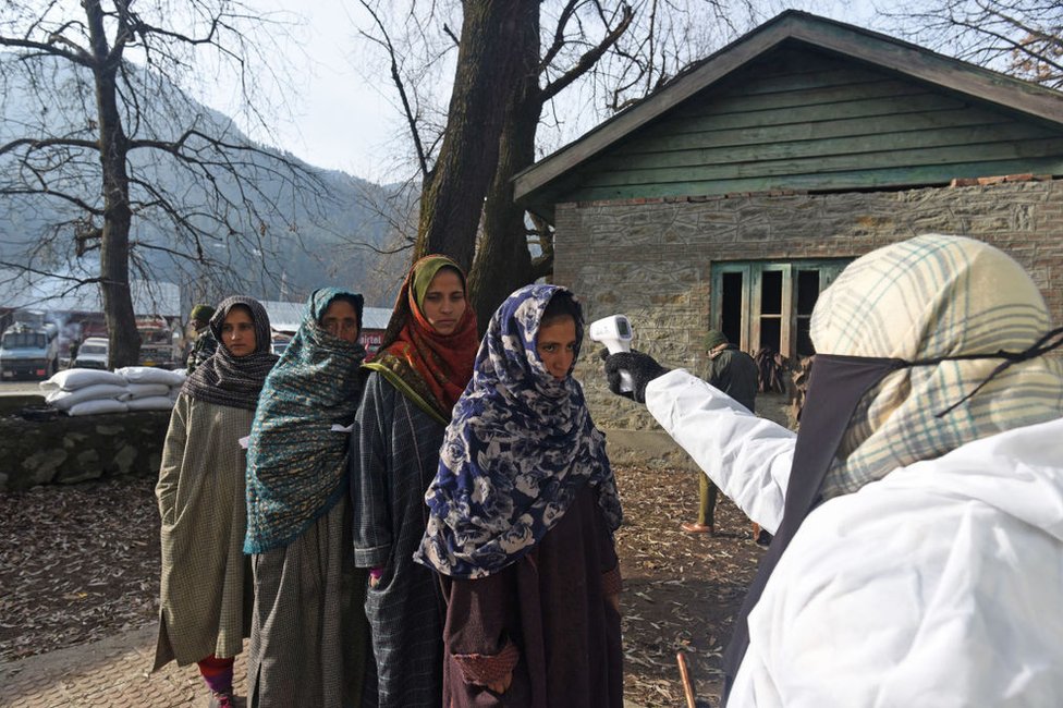 A health worker thermal screens voters arriving at a polling station to cast their vote.
