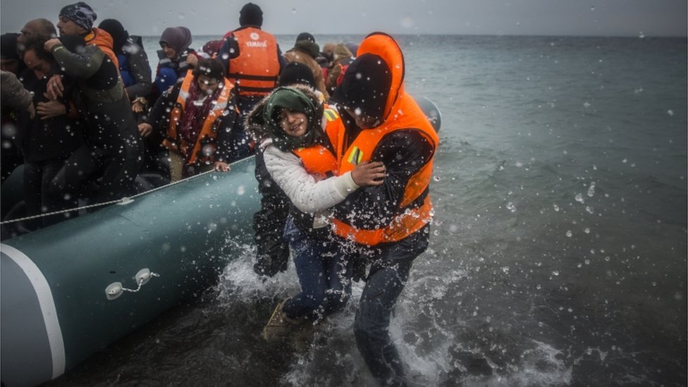 беженцев высаживают на берег с лодки