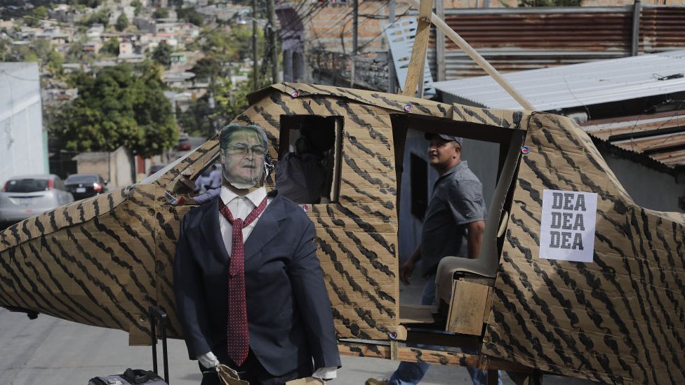 Figura de año viejo en las calles de Tegucigalpa mostrando al expresidente Juan Orlando Hernandez siendo transportado en un helicóptero de la DEA