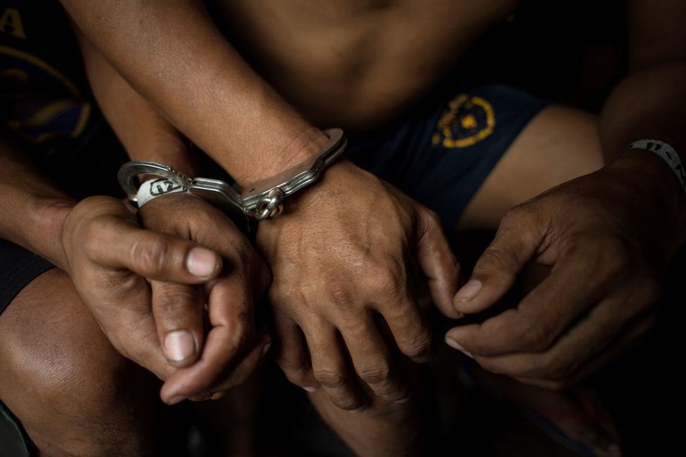 Жители мужского пола в наручниках собраны для проверки после того, как 20 июля 2017 года полицейские провели крупномасштабный рейд по борьбе с наркотиками в трущобах Манилы