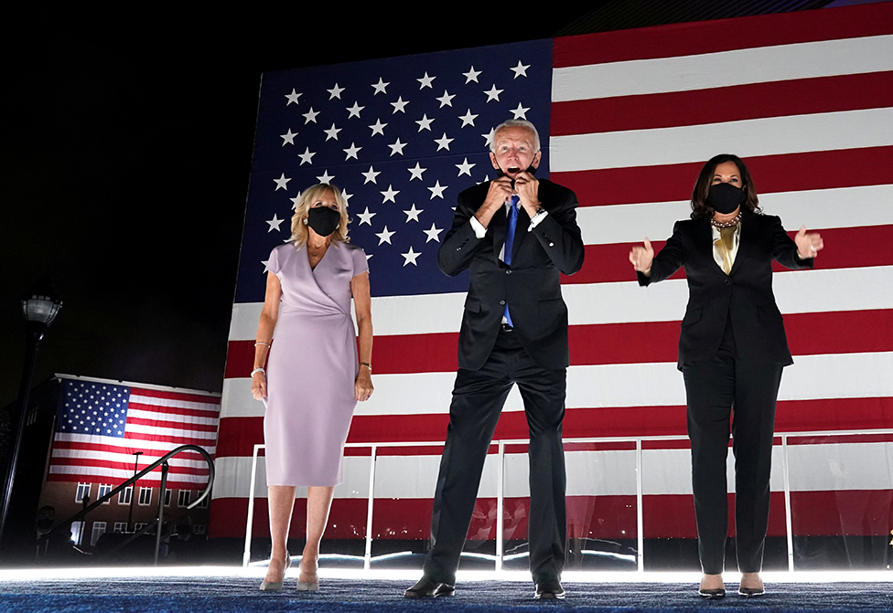 Joe Biden stands on stage with his wife Jill Biden and Kamala Harris with a giant US flag behind them