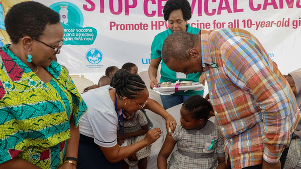 Президент Кении Ухуру Кениата смотрит на медсестру, которая делает инъекцию девочке