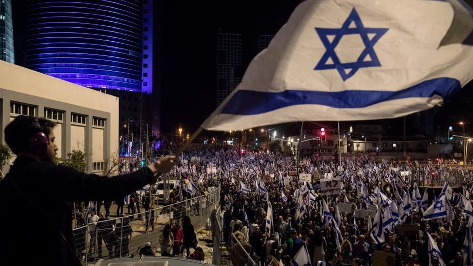A protester waves the Israeli flag during a massive protest against the government's judicial overhaul plan on 11 March 2023 in Tel Aviv