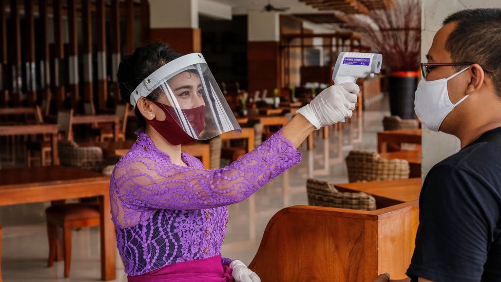 A woman in a restaurant in Bali, Indonesia, takes a customer's temperature