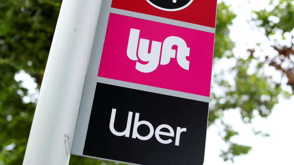 На этой фотографии видна вывеска с логотипами Lyft и Uber на автобусной остановке