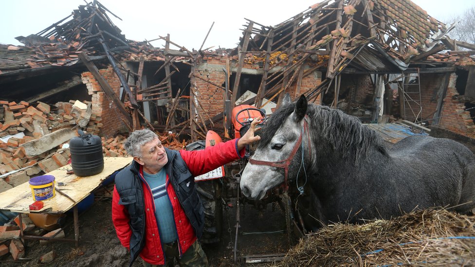 Farmer Tomislav Suknaic touches his horse in front of his damaged household in Majske Poljan village