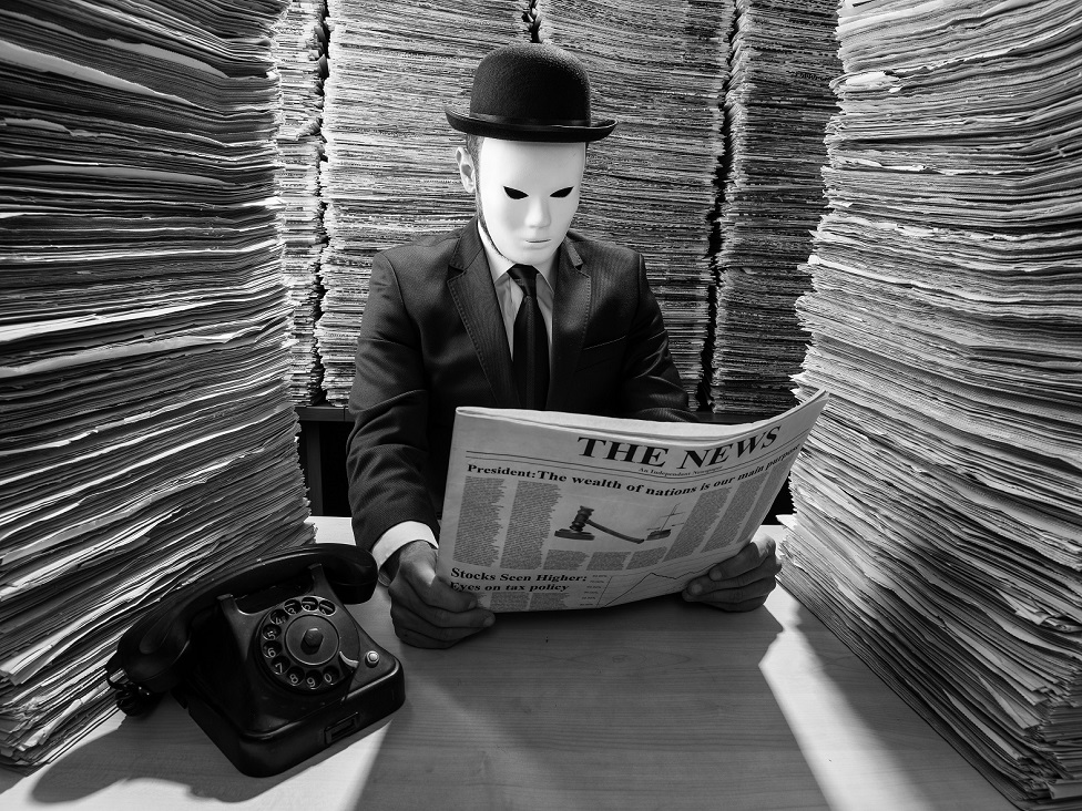 A man wearing a mask reads a newspaper