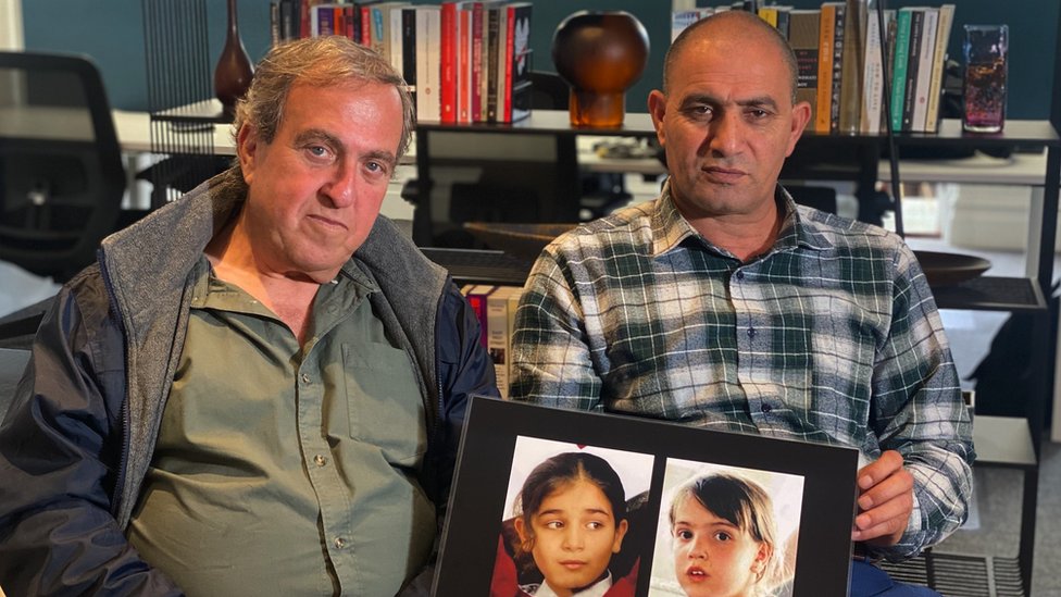 Bassam Aramin (left), and Rami Elhanan (right) sitting and holding a picture of their daughters