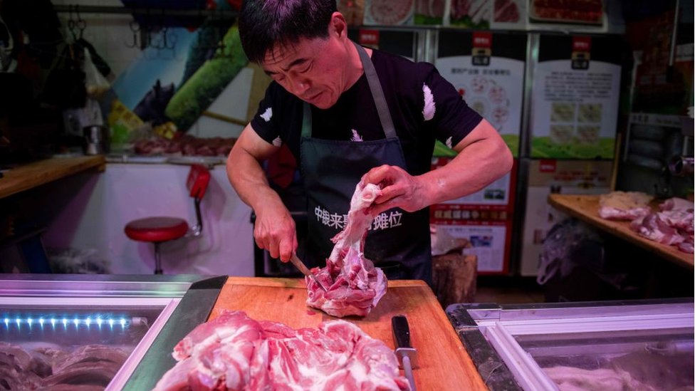На этом снимке, сделанном 10 июля 2019 года, мясник отрезает кусок свинины у своего прилавка на рынке в Пекине