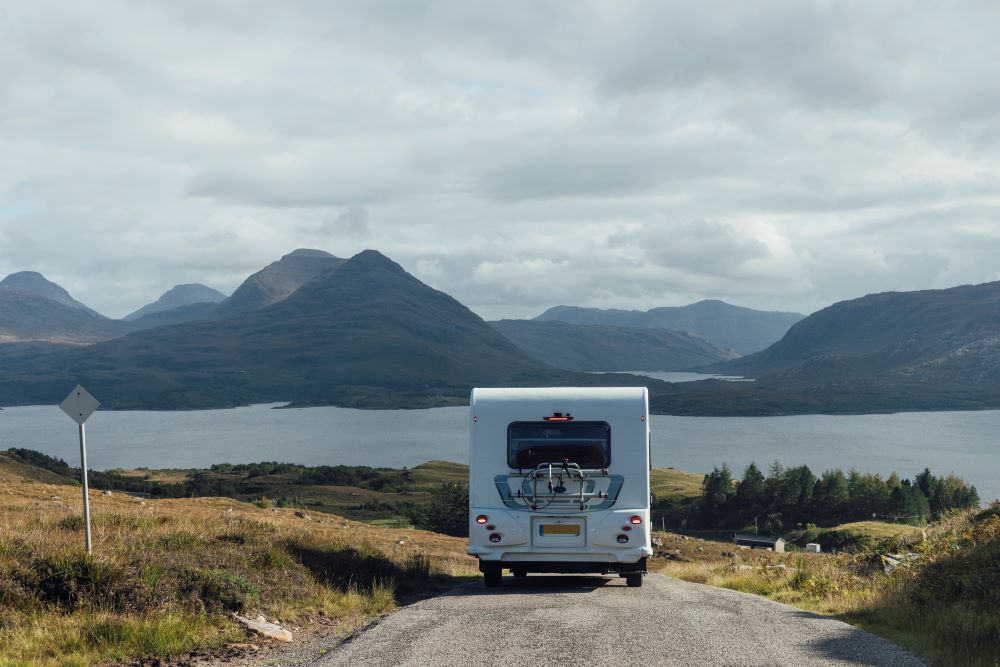 Campervan on a road in the Highlands, with a loch and mountains in background