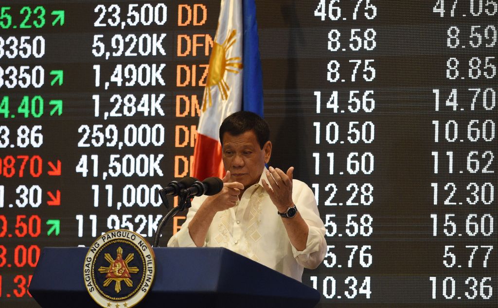 Philippine President Rodrigo Duterte mimics holding a rifle as he speaks in front of a stocks information board at the Philippine Stock Exchange