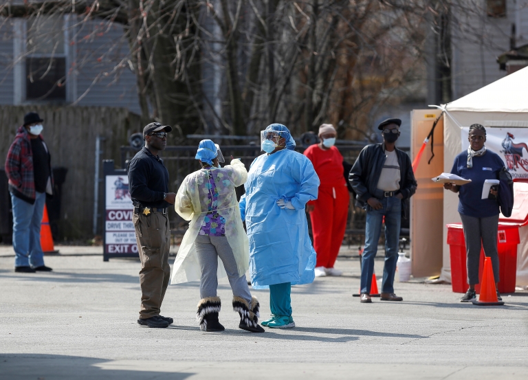 Medical workers talk as people waiting in line to receive testing  outside Roseland Community Hospital in Chicago, Illinois, 7 April 2020