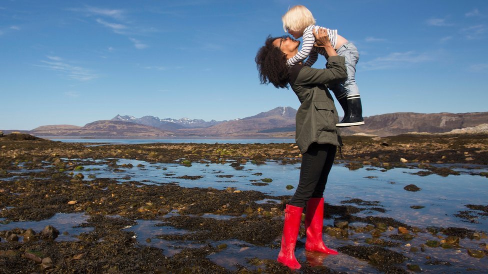 A mum lifting up and kissing her child with Highland scenery in the background.