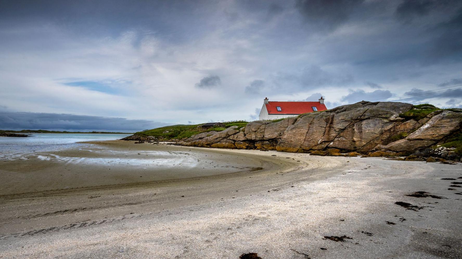 A red roofed cottage beside a beach in Barra in the Western Isles.