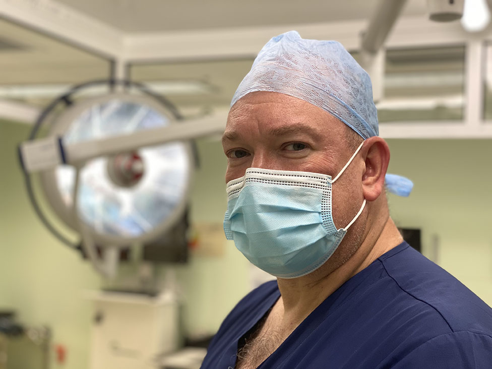 a doctor in an empty operating room wearing scrubs and a mask