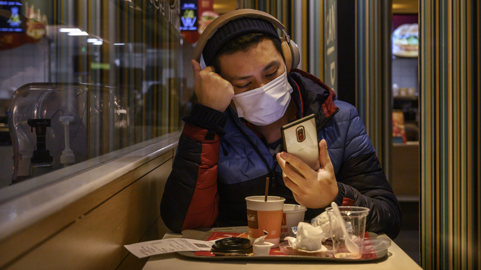 Man with a face mask checks phone while eating