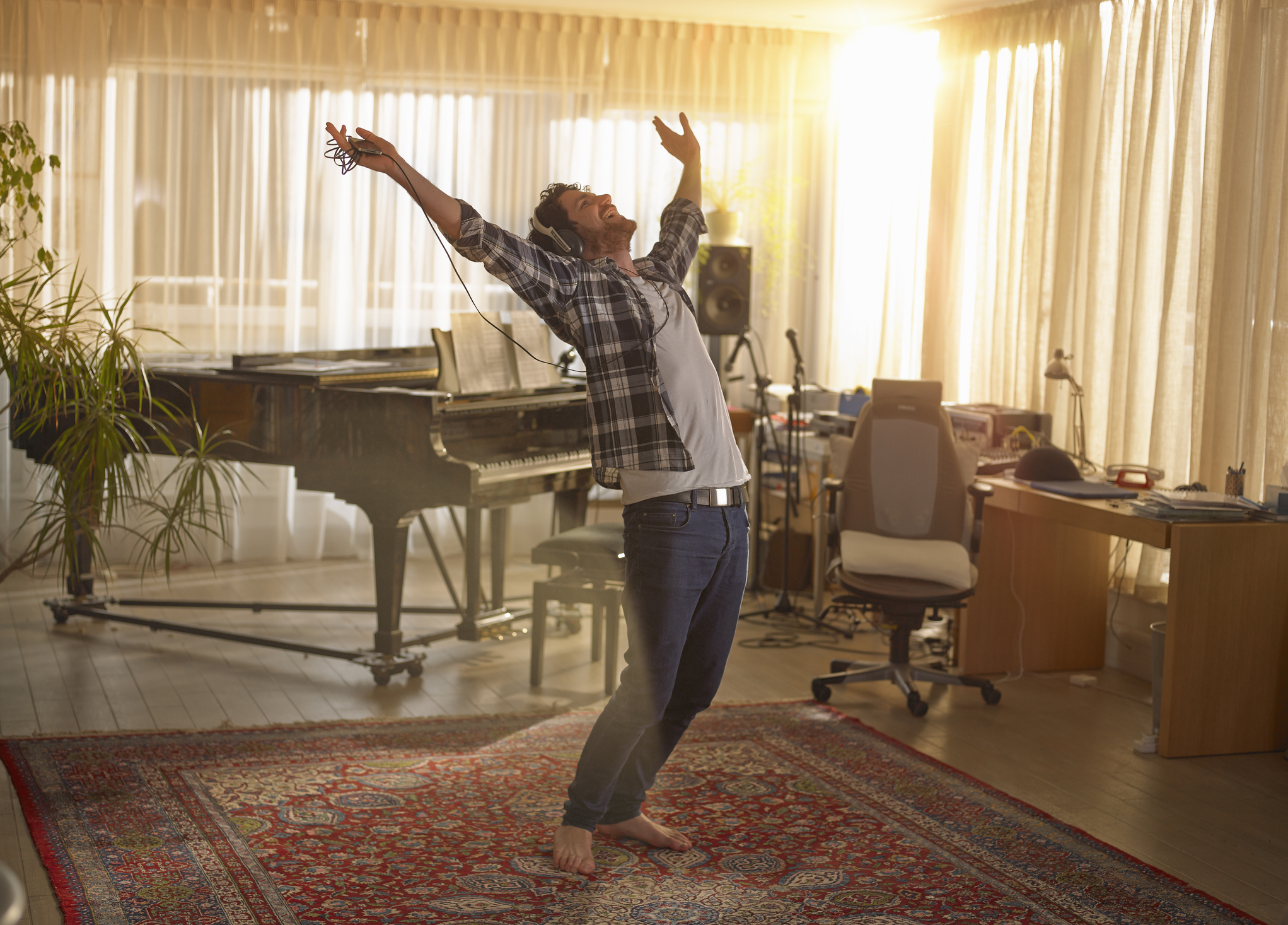 Un hombre frente a un piano y un escritorio levantando los brazos en una expresión de felicidad