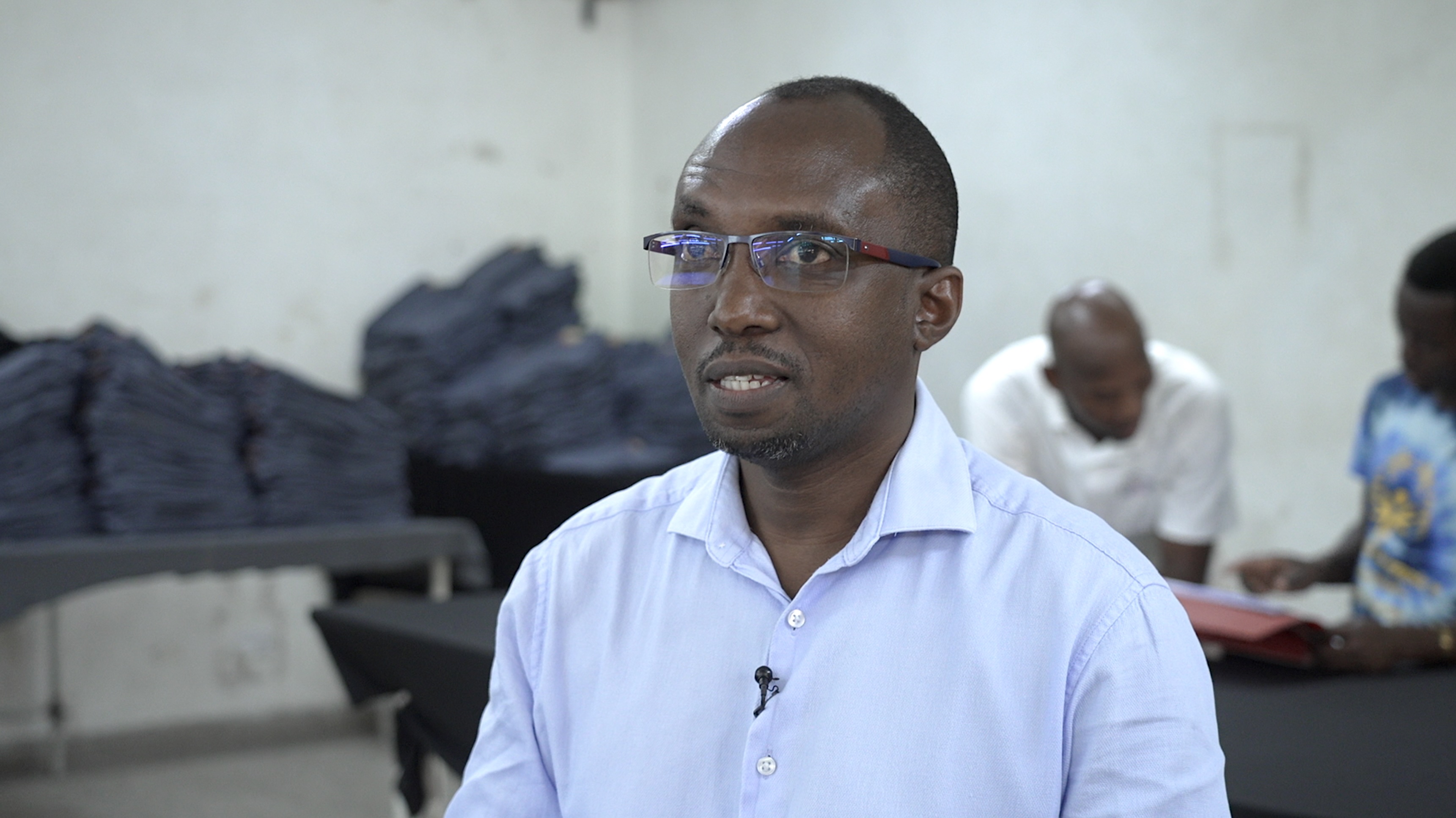 Isaac Maluki on the factory floor wearing an open-necked blue shirt. 