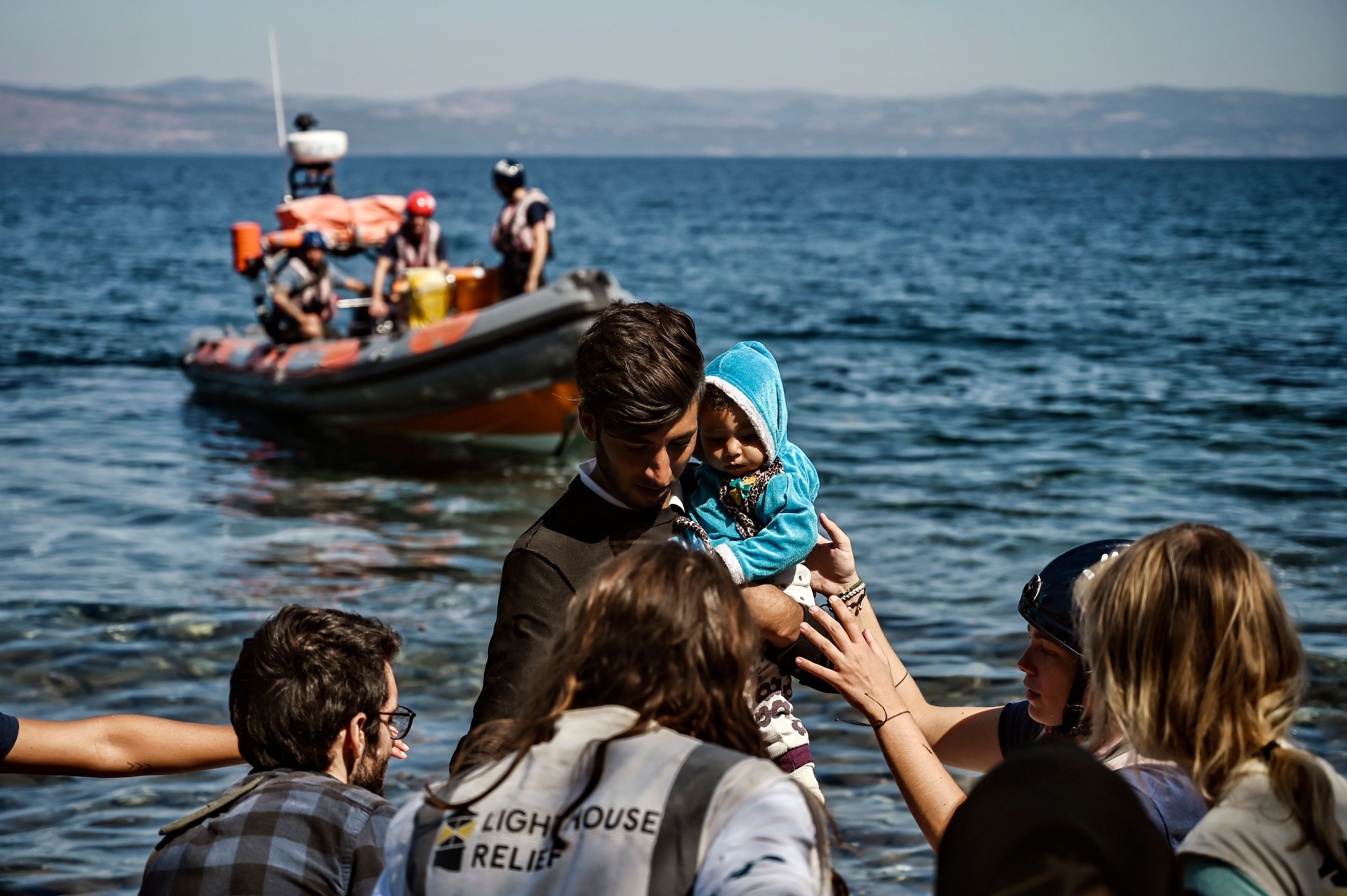 A migrant with a child is helped by rescuers as he arrives on the Greek island of Lesbos in September 2019