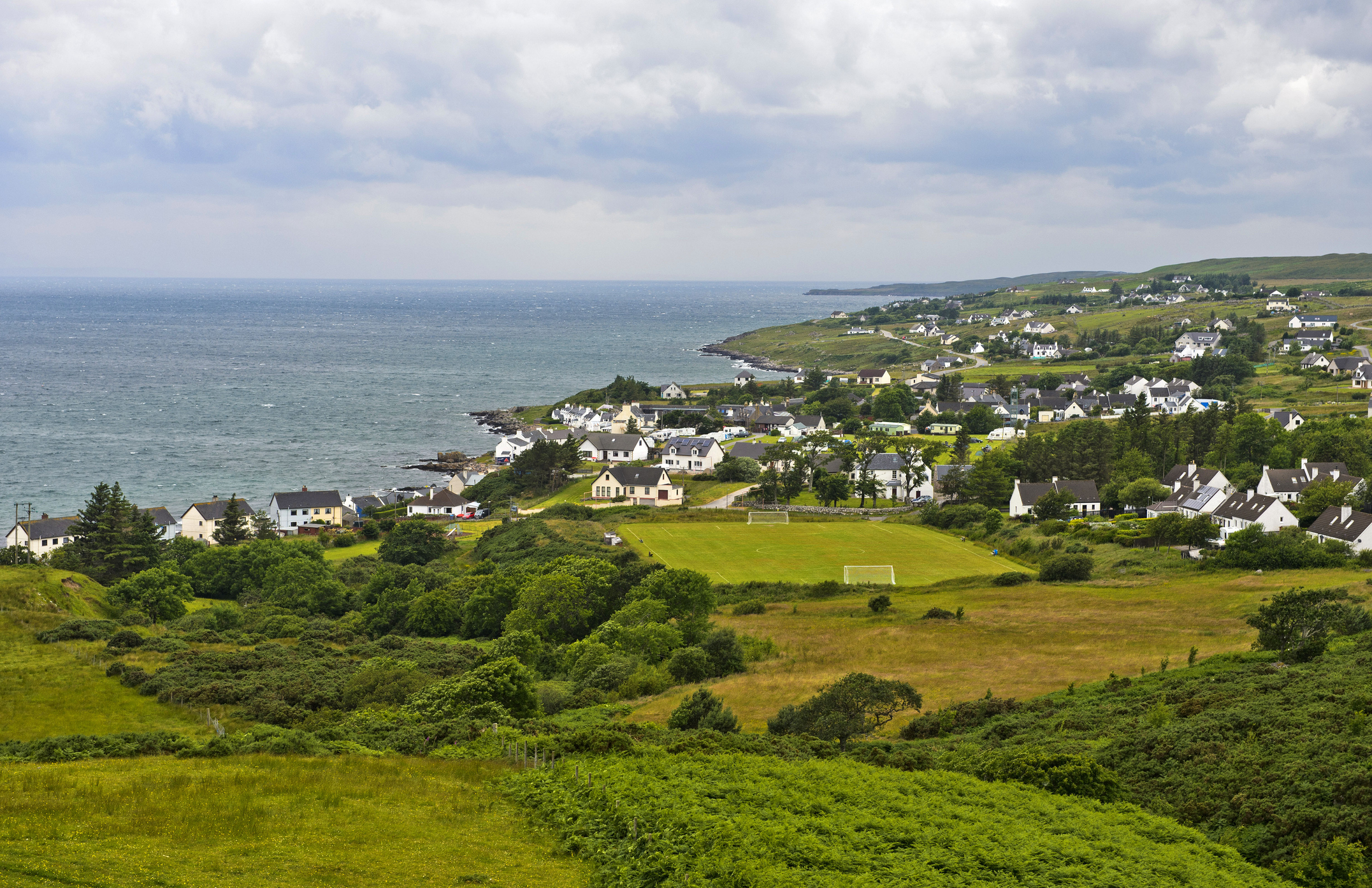 White-walled house set among fields and near the sea in Wester Ross.