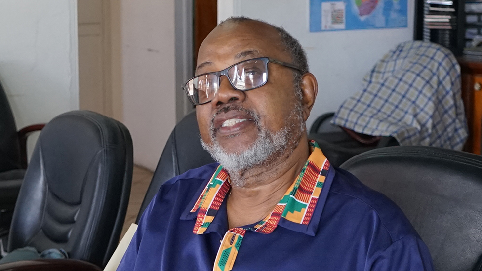A head and shoulders image of Dorbrene O'Marde, he is wearing a blue shirt with a collar made form Ghanaian kente cloth