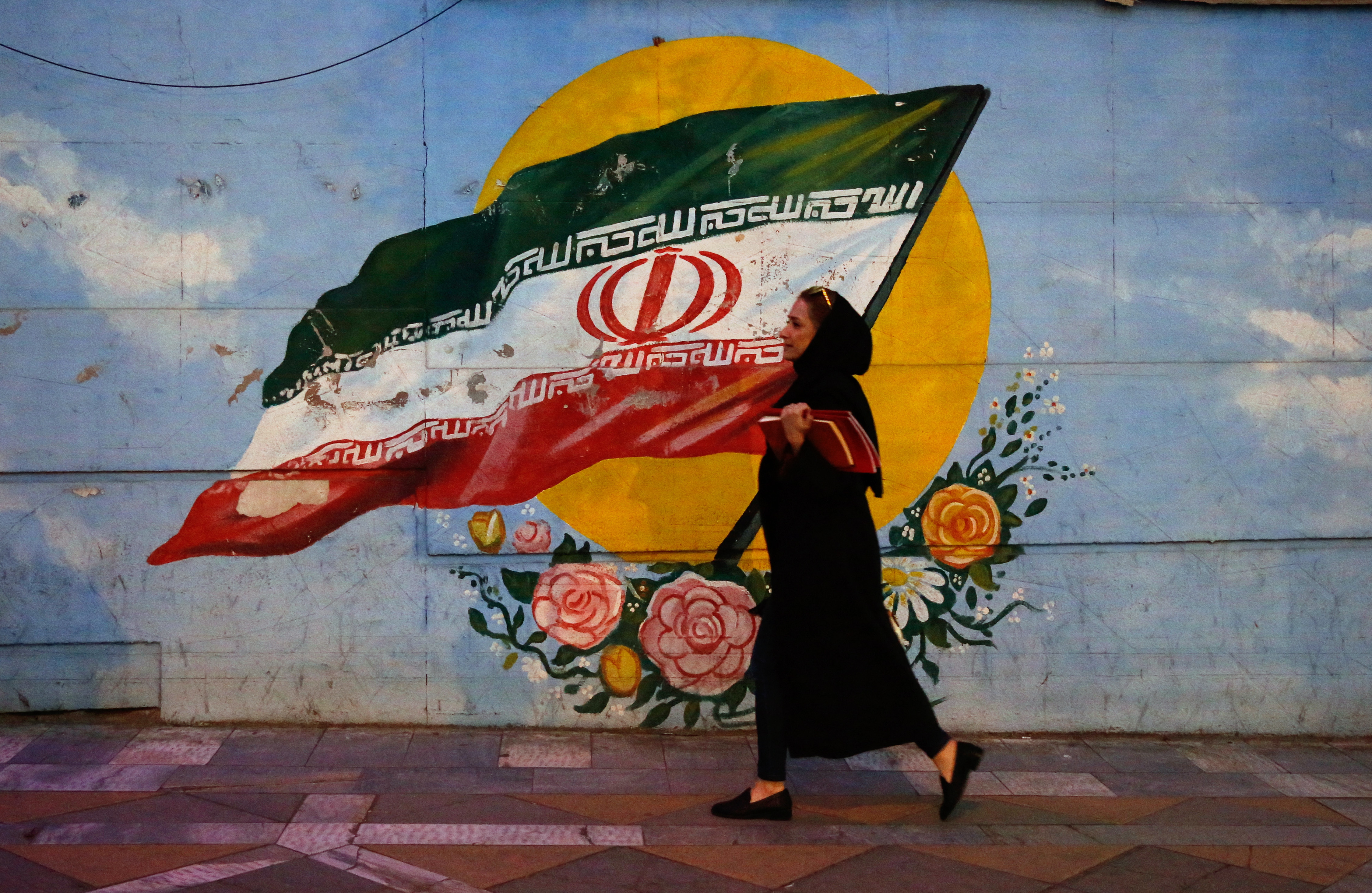 A woman walking past image of Iranian flag in Tehran