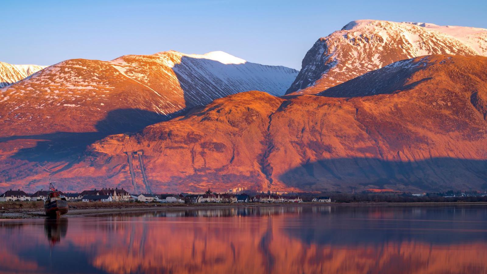 Houses line the shore of Loch Linnhe below Ben Nevis and nearby mountains.