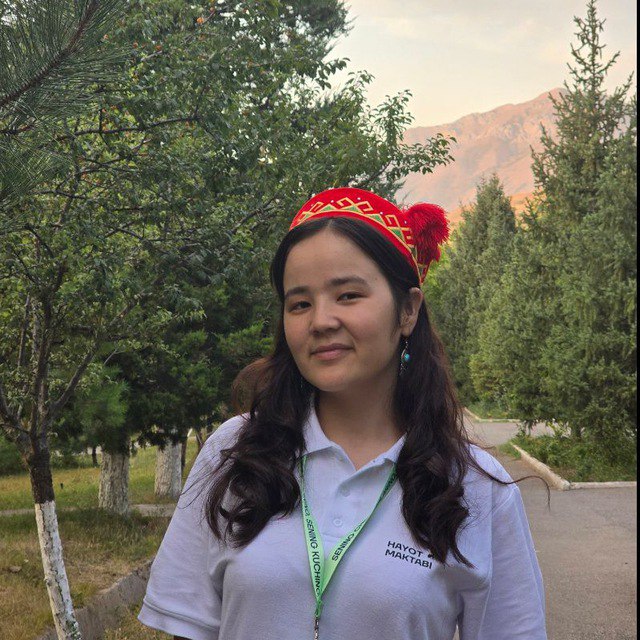 Qizil do'ppi kiygan qiz jilmayib turibdi