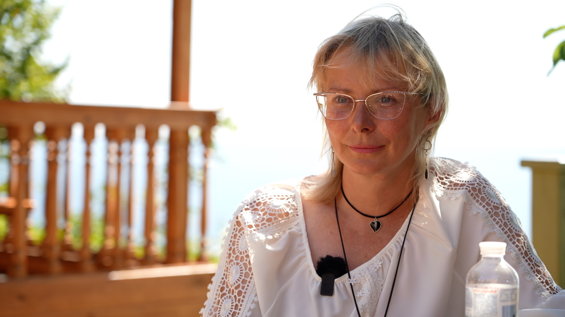 Svitlana Halchenko sits in a white shirt and glasses on a wooden deck overlooking the sea. 