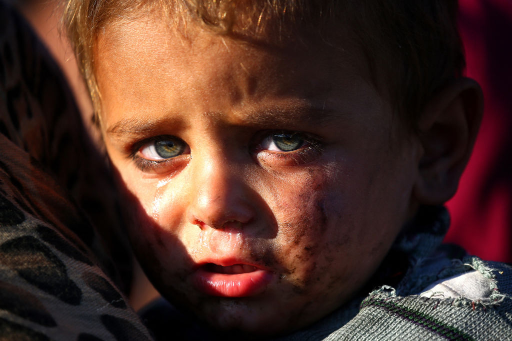 A Syrian boy cries as he is being held at a temporary refugee camp