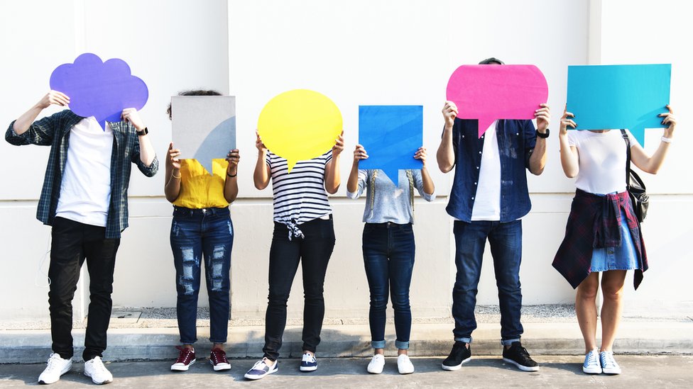 Una fila de personas están paradas una al lado de la otra con cartulinas que simulan nubes de conversación como las de los cómics