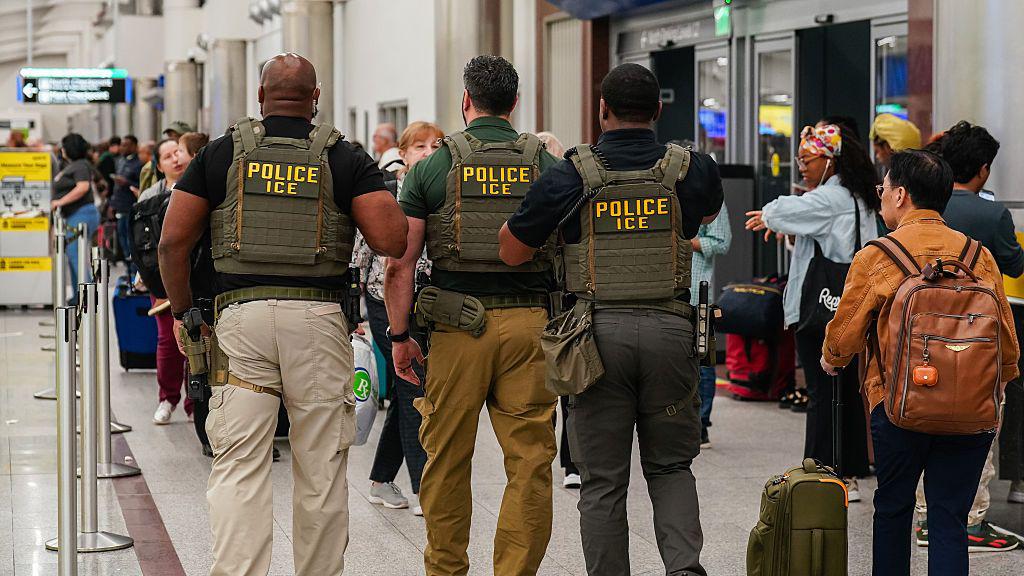 An ICE officer stands near crowded airport security lines during the Homeland Security shutdown.
